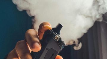 person holding black vape surrounded by smoke